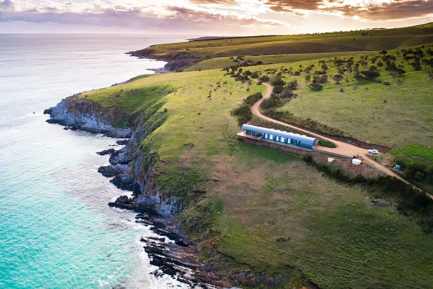 Naiko Retreat seen from the air, a low linear building following the ridgeline above a turquoise cove on the Fleurieu coast