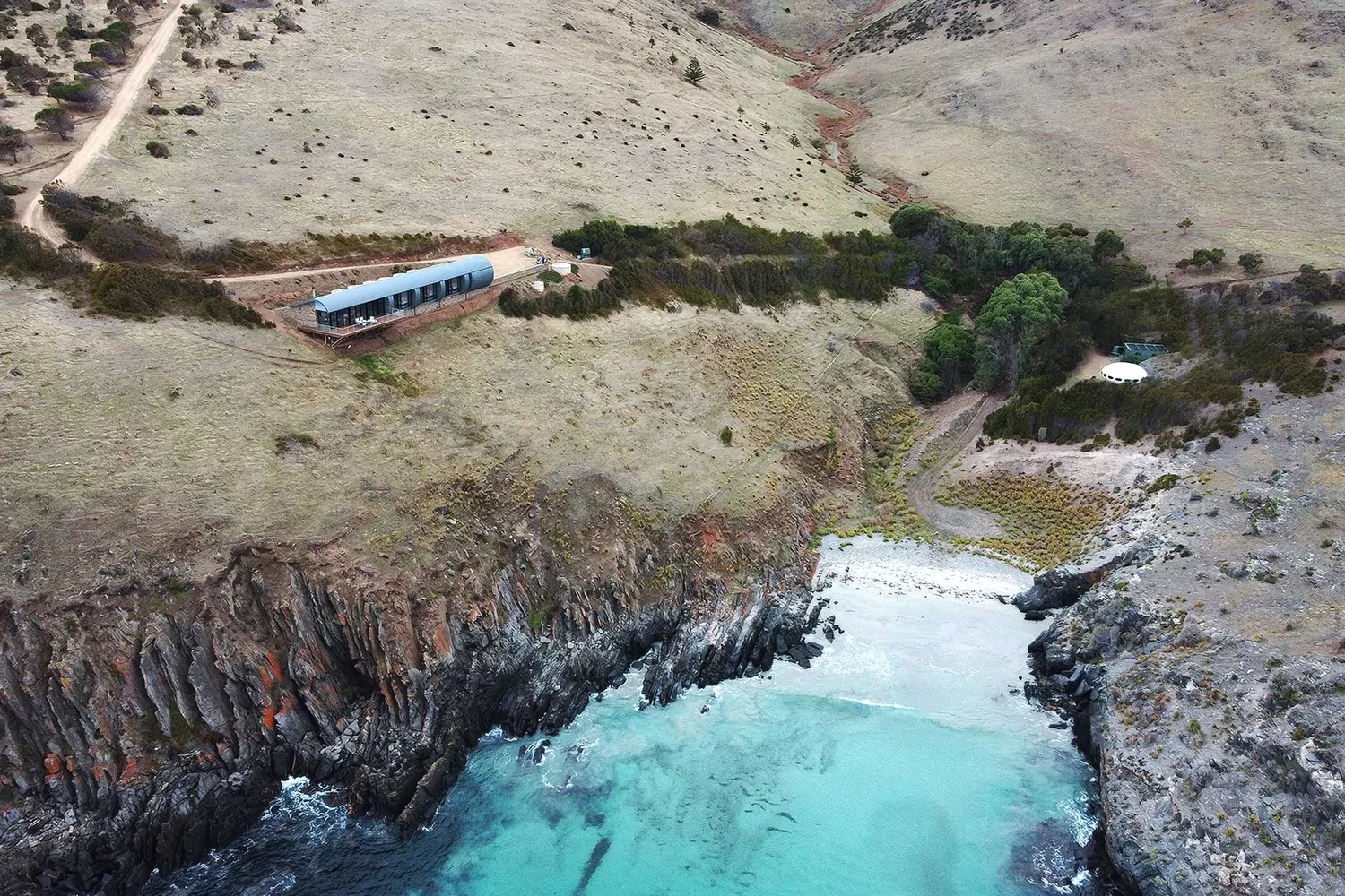 Aerial view of the secluded cove and clear aquamarine water below Naiko Retreat