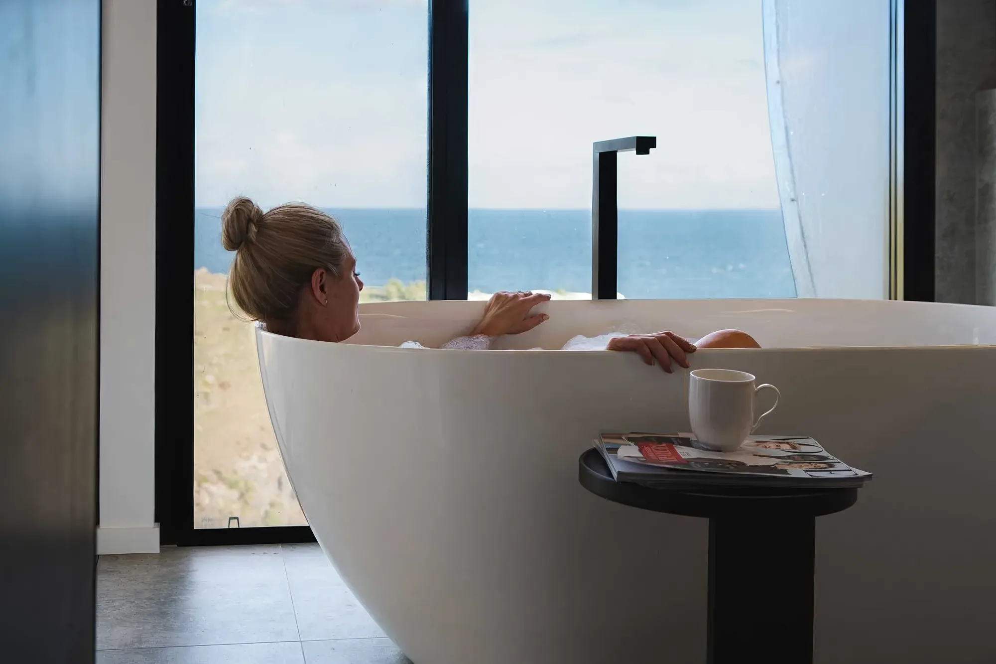 A guest soaking in the bath with the ocean beyond the window