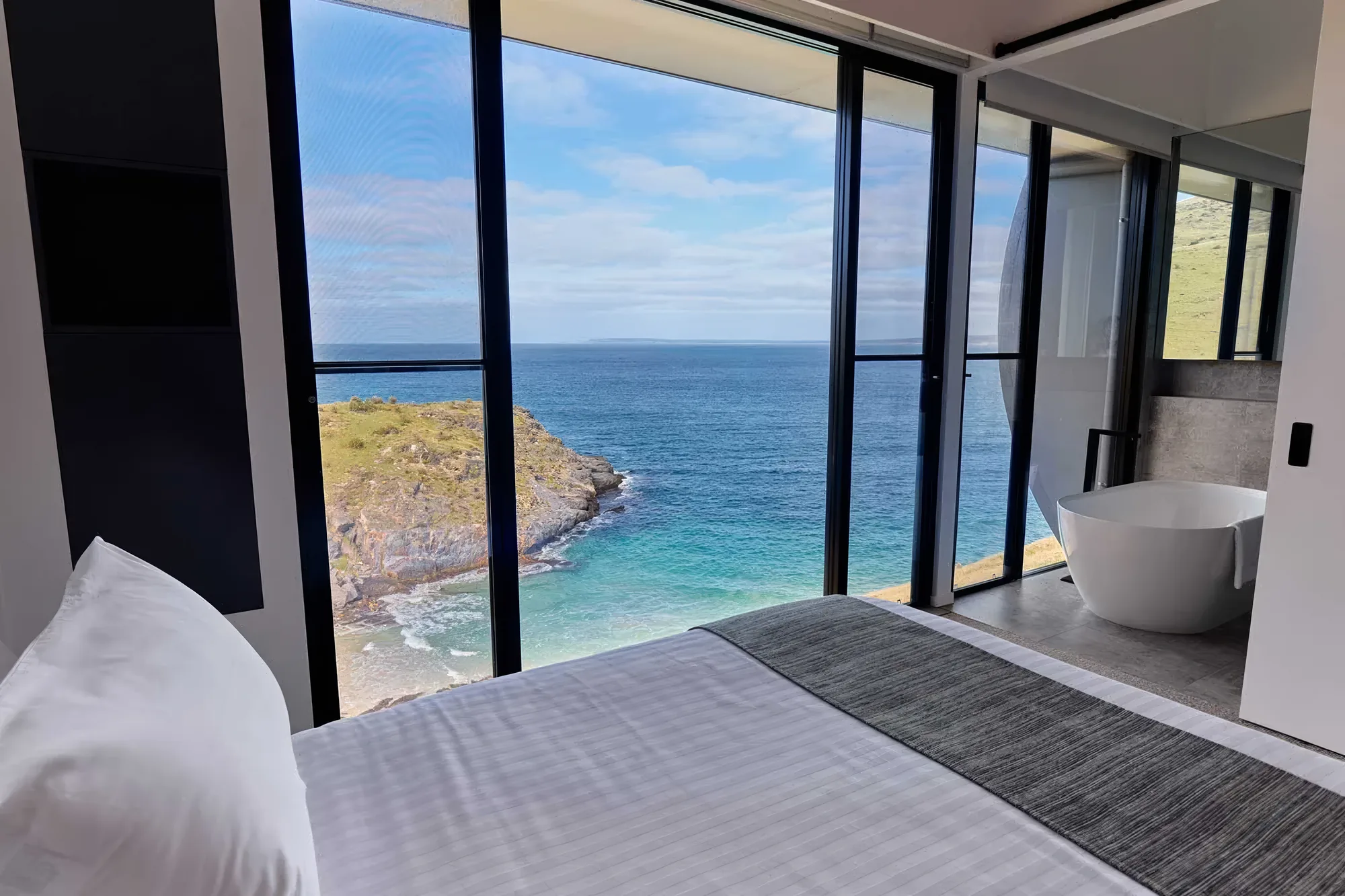 A king bed facing full-height glass above the turquoise cove