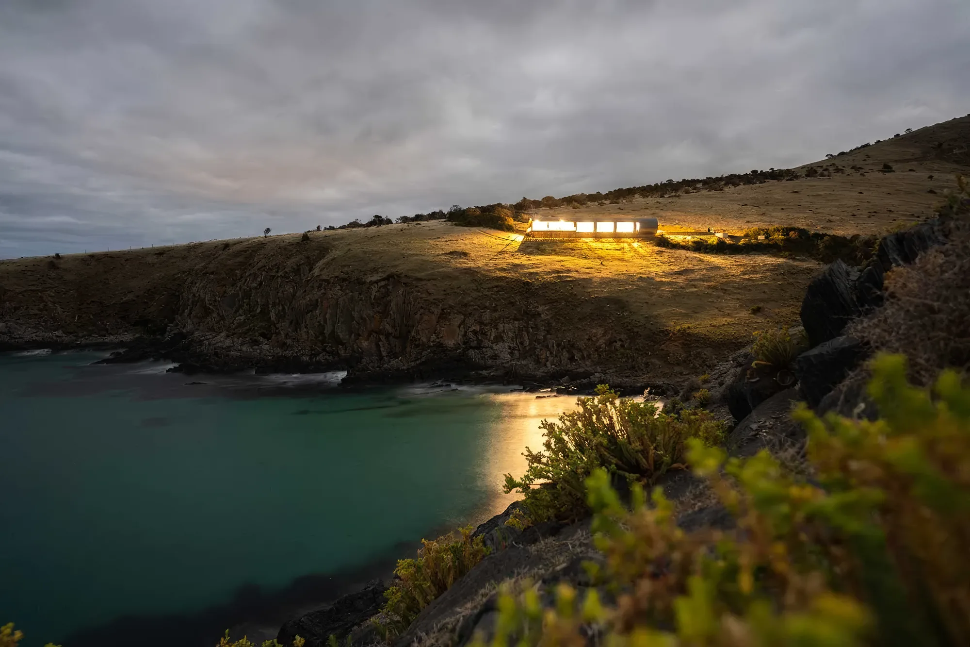 The cove below the retreat at night, lit along the shoreline