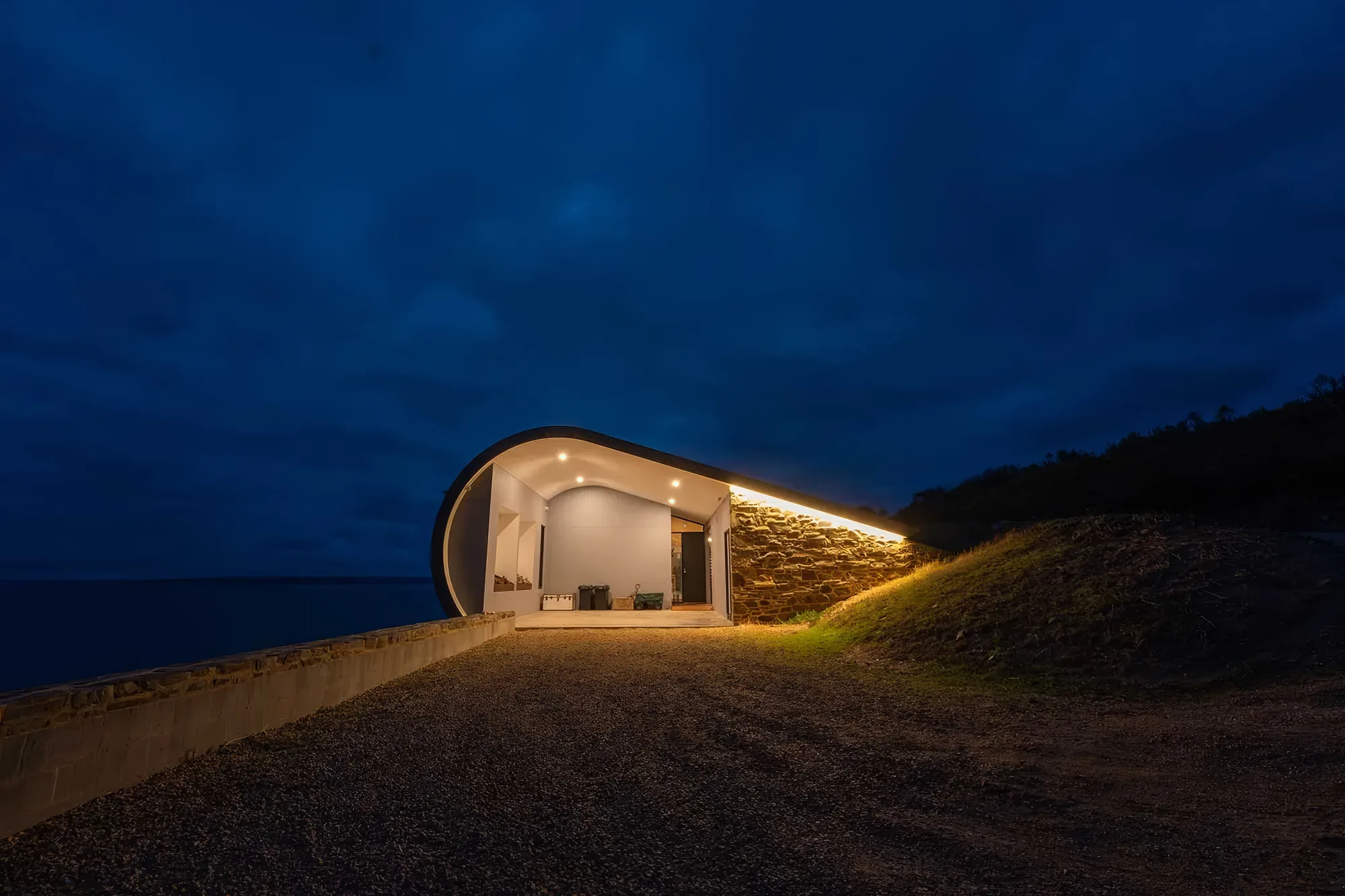Naiko Retreat lit from within at blue hour, its curved roof following the hillside
