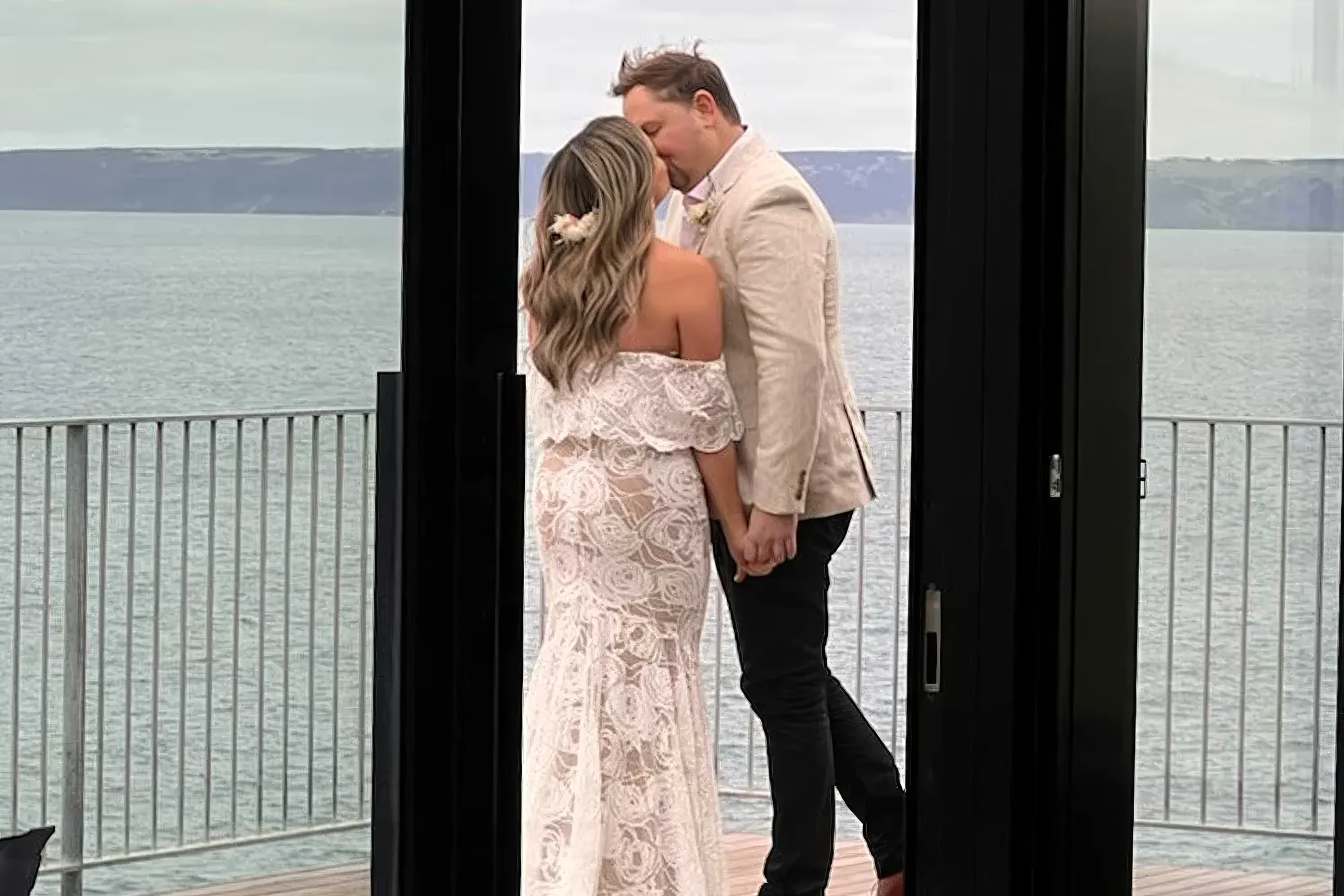 A couple at Naiko Retreat framed by the glass doors and the sea