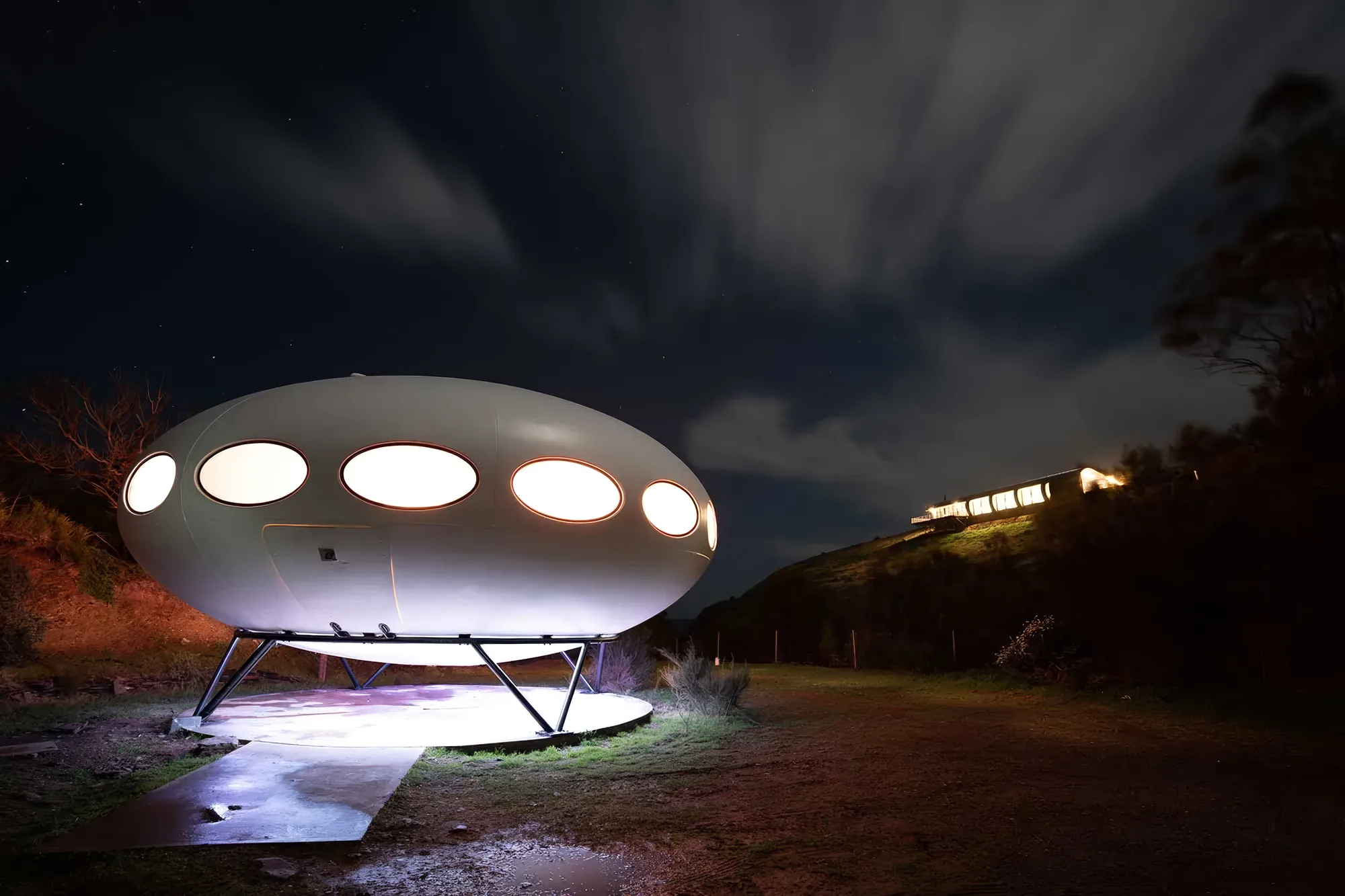 The Futuro house lit at night among the she-oaks